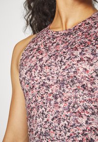 Top atlético com padrão roxo e rosa, de gola alta e tecido texturado, apresentando um design justo e uma estampa moderna e abstrata.