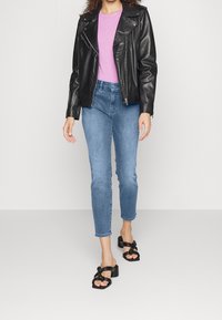 Chaqueta de moto de cuero negro, camiseta rosa, jeans de mezclilla azul claro y sandalias negras de tacón con detalle de nudo. Diseño de outfit simple y moderno.