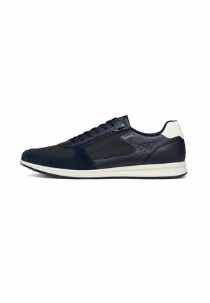 Zapatilla deportiva de hombre de caña baja en azul marino con parche blanco en el talón, cordones delanteros, cremallera lateral y suela blanca.