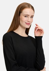 Pull en mailles noir avec un col rond, des manches longues et des poignets côtelés. Texture lisse et coupe ajustée, mettant en avant un style minimaliste.