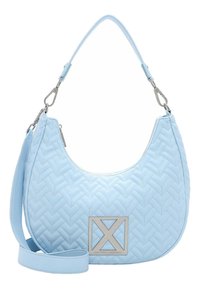 Sac à bandoulière matelassé bleu clair avec anse amovible et bandoulière croisée, fermeture éclair argentée, et plaque métallique carrée avec logo sur le devant.