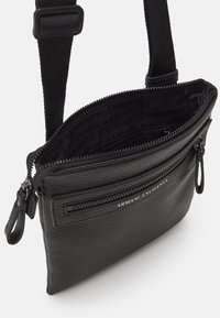 Borsa a spalla nera in pelle con superficie texture, tasca con zip e tracolla regolabile. L'interno presenta un motivo ripetuto con il logo.