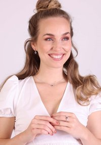 Ensemble de bijoux en argent ornés de pierres bleues en forme de cœur, comprenant des boucles d'oreilles, un collier et une bague, portés par un modèle aux longs cheveux.