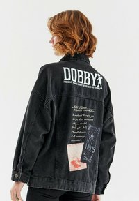 Czarna dżinsowa kurtka z nadrukami tekstowymi i graficznymi na plecach, w tym logo "DOBBY" oraz ilustracje przypominające karty i odręczne notatki.