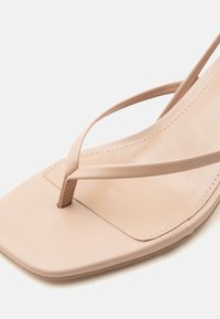 Μπεζ σανδάλι με τετράγωνη μύτη, λεπτές λουρίδες που διασταυρώνονται μπροστά και ραμμένη δερμάτινη σόλα.