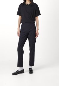 Black short-sleeve t-shirt paired with navy slim-fit trousers and black loafers. Accessories include a gold chain necklace.