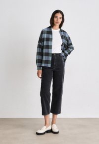 Geruite flanellen overhemd in blauw en zwart, wit T-shirt, zwarte corduroy capri-broek en roomkleurige loafers met een dikke zool.