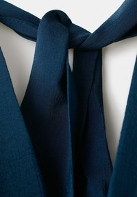 Posnetek iz bližine temno modre pletene kravate, prepletene v preprosto vozlišče na enostavni podlagi.