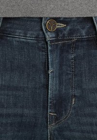 Donkerblauwe denim jeans met een rits met knoopsluiting, subtiele vervaging en contrasterende stiksels langs de naden.