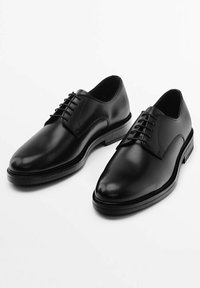 Scarpe eleganti in pelle nera con una texture liscia, punta arrotondata e chiusura con lacci. Presentano una suola in gomma a profilo basso e dettagli minimi.
