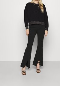 Czarna krótka bluza z fakturowanym paskiem, w połączeniu z czarnymi spodniami w dzwony z bocznymi rozcięciami, uzupełniona czarnymi sandałkami na obcasie.