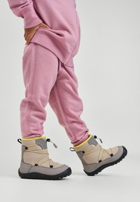 Szare buty trekkingowe z żółtymi akcentami, gumowymi podeszwami i elastycznymi sznurowadłami, zestawione z różowymi spodenkami dresowymi o luźnym kroju i prążkowanej fakturze.