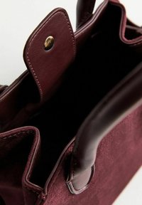 Borsa bordeaux con manici in pelle liscia e corpo in morbido suède. Caratterizzata da una chiusura magnetica e cuciture ordinate lungo i bordi.