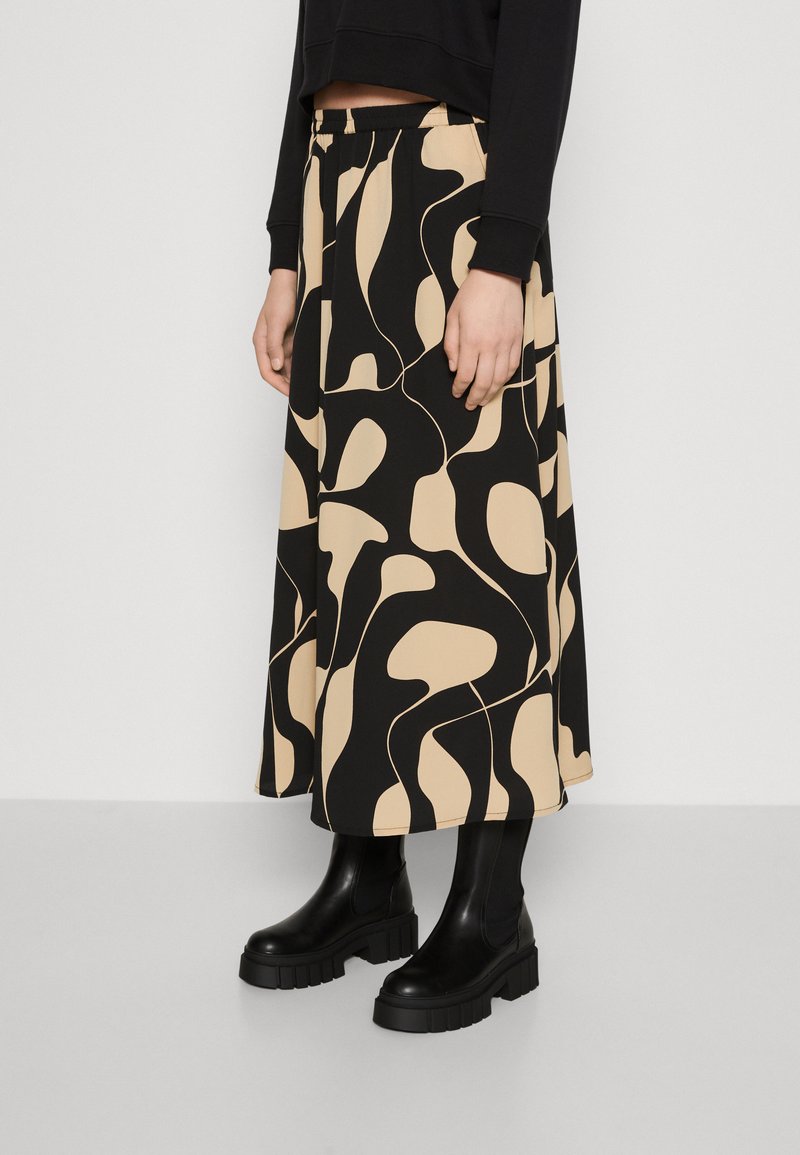 Saia padrão preta e bege com cintura elástica, feita de tecido leve; usada com botas de tornozelo pretas com solas grossas.