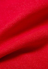 Nahaufnahme eines strukturierten roten Stoffes mit kleinem Strickmuster und sichtbaren Falten, die Schatten und Tiefe erzeugen.