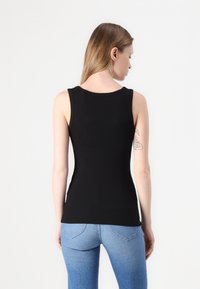 Top de tanque preto sem mangas em tecido elástico, apresentando um decote redondo e um design ajustado, combinado com jeans de ganga azul claro.