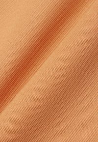 Gros plan sur un tissu couleur pêche montrant une texture délicatement tissée et des plis doux.