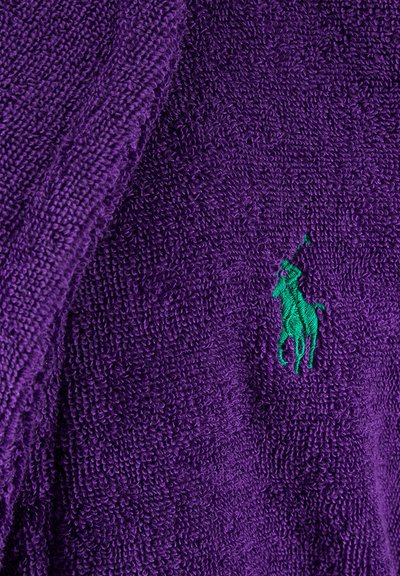 Serviette violette en tissu texturé, ornée d'un logo de polo brodé vert. Surface duveteuse avec une sensation de moelleux et des accents de couleur contrastants.