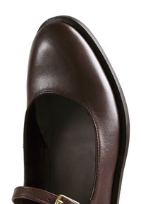 Chaussure Mary Jane en cuir marron avec embout arrondi, semelle noire et une petite boucle dorée sur la bride du cou-de-pied, isolée sur fond blanc.