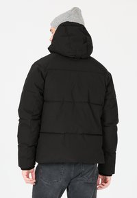 Svart vadderad jacka med huva, med horisontella sömmar, texturerad tyg och hög krage. Bärs med grå jeans och en ljusgrå mössa.