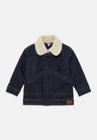 Chaqueta de mezclilla azul oscuro con cuello de sherpa crema, mangas largas, bolsillos frontales en ángulo y un parche de logo marrón cerca del dobladillo.