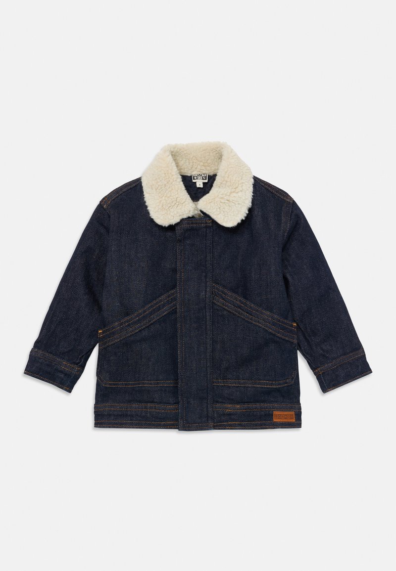 Dark blue denim jacket with cream sherpa collar, long sleeves, angled front pockets, and a brown logo patch near the hem.