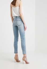 Sittande ljusblå jeans med en blekt design och bakfickor, i kombination med en vit ärmlös topp och nakna högklackade sandaler.