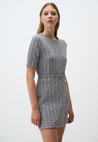 Abito a maniche corte con motivo a scacchi bianco e nero, caratterizzato da bottoni dorati sulle spalle, vestibilità sartoriale e tessuto testurizzato.