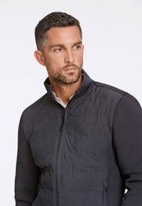 Mörkblå jacka med dragkedja framtill, kviltad frampanel och släta ärmar. Minimalistisk design med hög krage och inga synliga mönster.