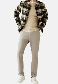 Zwart en beige geruite flanellen shirt over een beige t-shirt, gecombineerd met lichtgrijze broeken en witte sneakers. Eenvoudige, casual outfit.