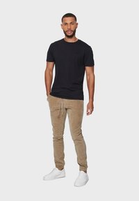 Zwarte katoenen t-shirt met korte mouwen, gecombineerd met lichtbruine corduroy joggers en witte sneakers, met een elastische tailleband en manchetten.