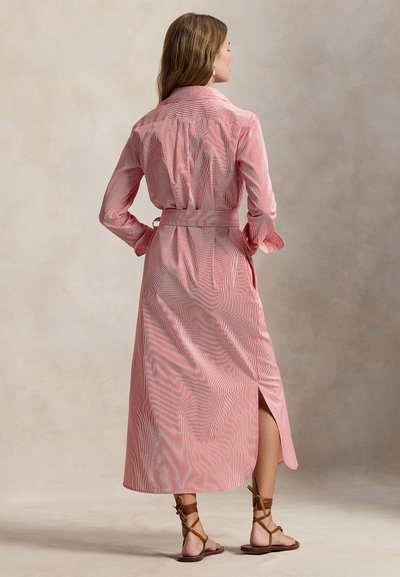 Μακρύ ροζ και λευκό ριγέ πουκάμισο-φόρεμα με ζώνη στη μέση, γιακά και λεπτομέρειες με κουμπιά, με μακριά μανίκια και ανοίγματα στα πλαϊνά στο τελείωμα.