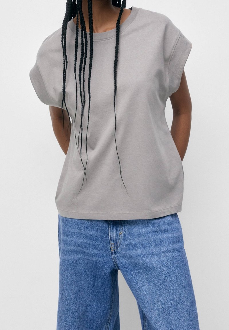 Un haut gris à manches courtes en tissu doux, avec une coupe décontractée et un col rond, associé à un jean large bleu clair.