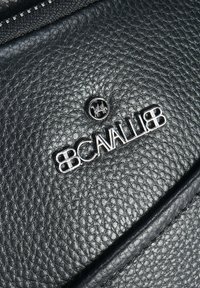 Surface en cuir noir avec une finition texturée, comportant un logo et un accent en argent. Détail de fermeture éclair visible le long du bord supérieur.