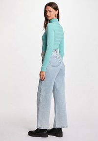 Pull en col roulé ajusté teal clair avec des rayures horizontales, associé à un jean taille haute bleu clair à jambes larges et des bottes noires volumineuses.