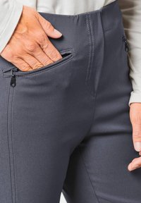 Dunkelgraue Hosen mit einer glatten Textur, ausgestattet mit Reißverschluss-Seitentaschen und detaillierten Nähten entlang der Säume. Der Stoff wirkt dehnbar.