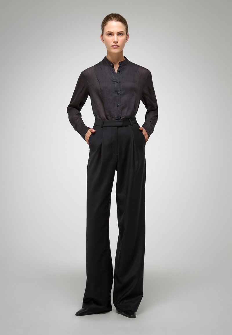 Blouse noire à boutons avec un col mandarin, associée à un pantalon large à taille haute noir. Tissu lisse et design structuré.