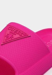 Φωτεινό ροζ σανδάλι slide με υφή στη λουρίδα που διαθέτει ανασηκωμένη τριγωνική λογότυπο Guess και σχέδιο με φοίνικα.