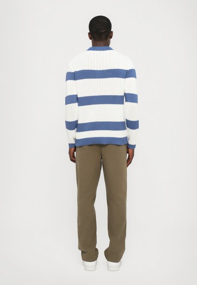 Strikket genser med blå og hvite striper, ribbet tekstur og krage, sammen med beige bukser og hvite sneakers. Bakvinkel.