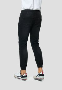 Czarne spodnie dresowe z elastyczną talią i ściągaczami, wyposażone w pięć kieszeni i o dopasowanym kroju, zestawione z wielokolorowymi sneakerami.