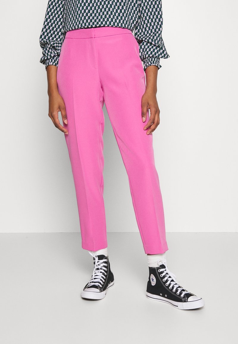 Pantalons sur mesure roses en tissu lisse, avec une taille mi-haute et des jambes fuselées, associés à des baskets montantes noires.