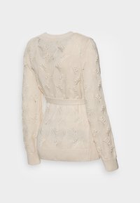Kremowy sweter z dzianiny z misternym wzorem fal, z długimi rękawami i przewiązanym paskiem. Teksturowane wykończenie dodaje głębi; okrągły dekolt.