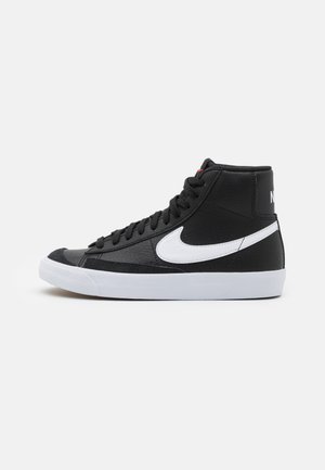 Baskets montantes noires avec semelle blanche et logo Nike swoosh, lacets noirs et détails en cuir texturé, vue de côté sur fond uni.