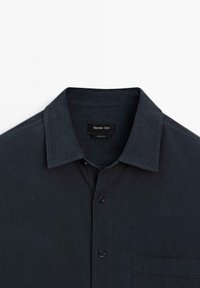 Camicia blu scuro con bottoni, caratterizzata da un colletto strutturato, taschino sul petto e una sottile texture. L'etichetta riporta "Massimo Dutti."