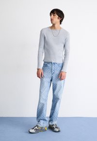 Lys grå ribbet langermet topp kombinert med lys blå mønstrede jeans og grå joggesko med gule detaljer, stylet med et tynt halskjede.