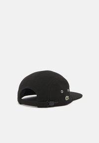 Sort baseball cap lavet af stof, med en flad skygge, justerbar rem bagpå, og et lille broderet krokodillelogo på forsiden.