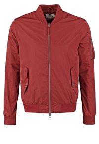Veste bomber rouge avec fermeture éclair devant, deux poches à pression, poche zippée sur la manche gauche, et col, poignets et ourlet côtelés.