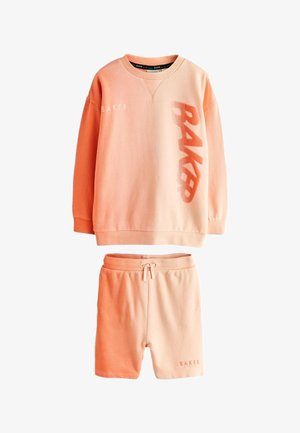 Perzikkleurige trui met lange mouwen met "BAKER" en shorts met aantrekkoord en tekst "BAKER" linksonder.
