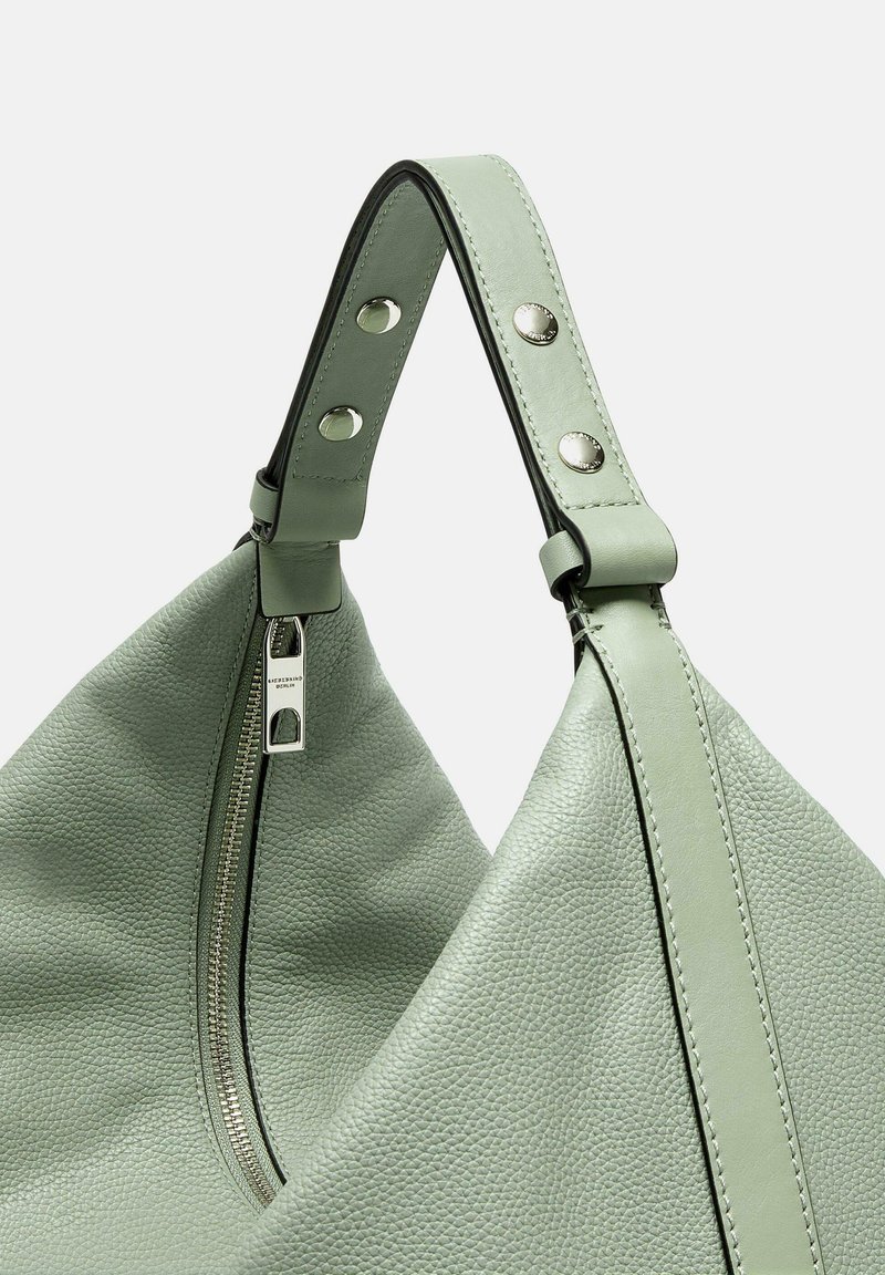 Grüne Lederhandtasche mit strukturiertem Oberflächenfinish, ausgestattet mit einem silbernen Reißverschluss und genietetem Riemenakzenten. Dreieckige Form mit einem gebogenen Griff.