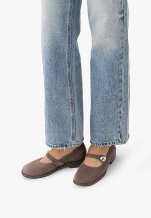 Stopy w szarych zamszowych butach Mary Jane z okrągłą srebrną sprzączką, w połączeniu z jasnoniebieskimi prostymi dżinsami o postrzępionych nogawkach.